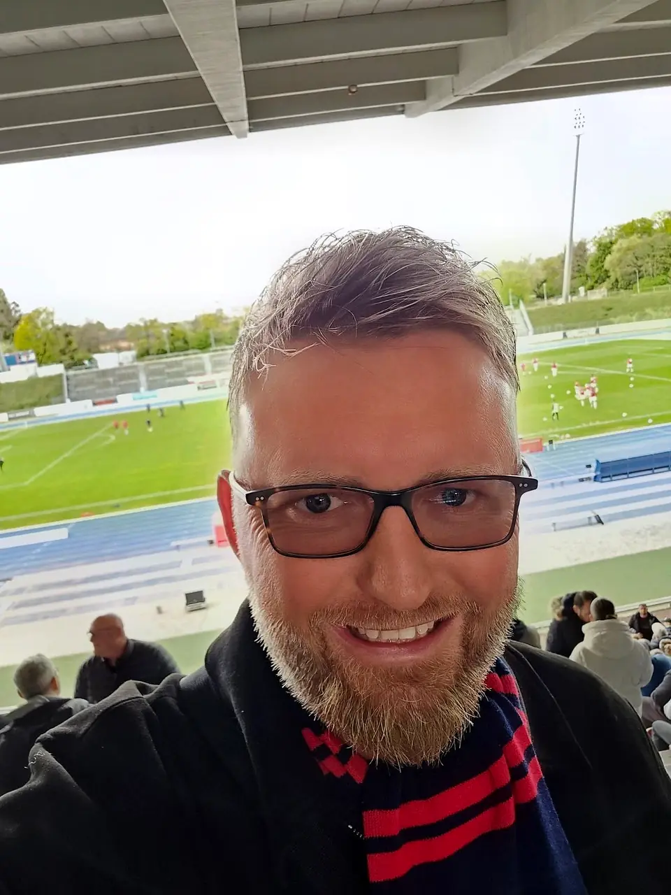 Sascha Frenz lächelt auf der Tribüne mit Blick auf das Spielfeld.
