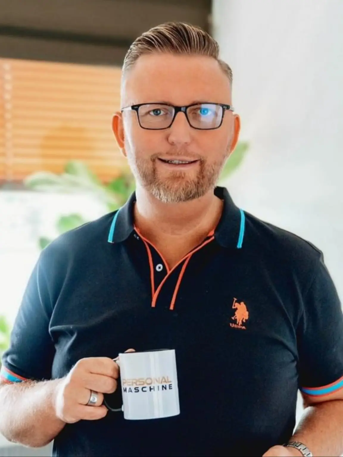 Sascha Frenz hält lächelnd eine Tasse der Personalmaschine.